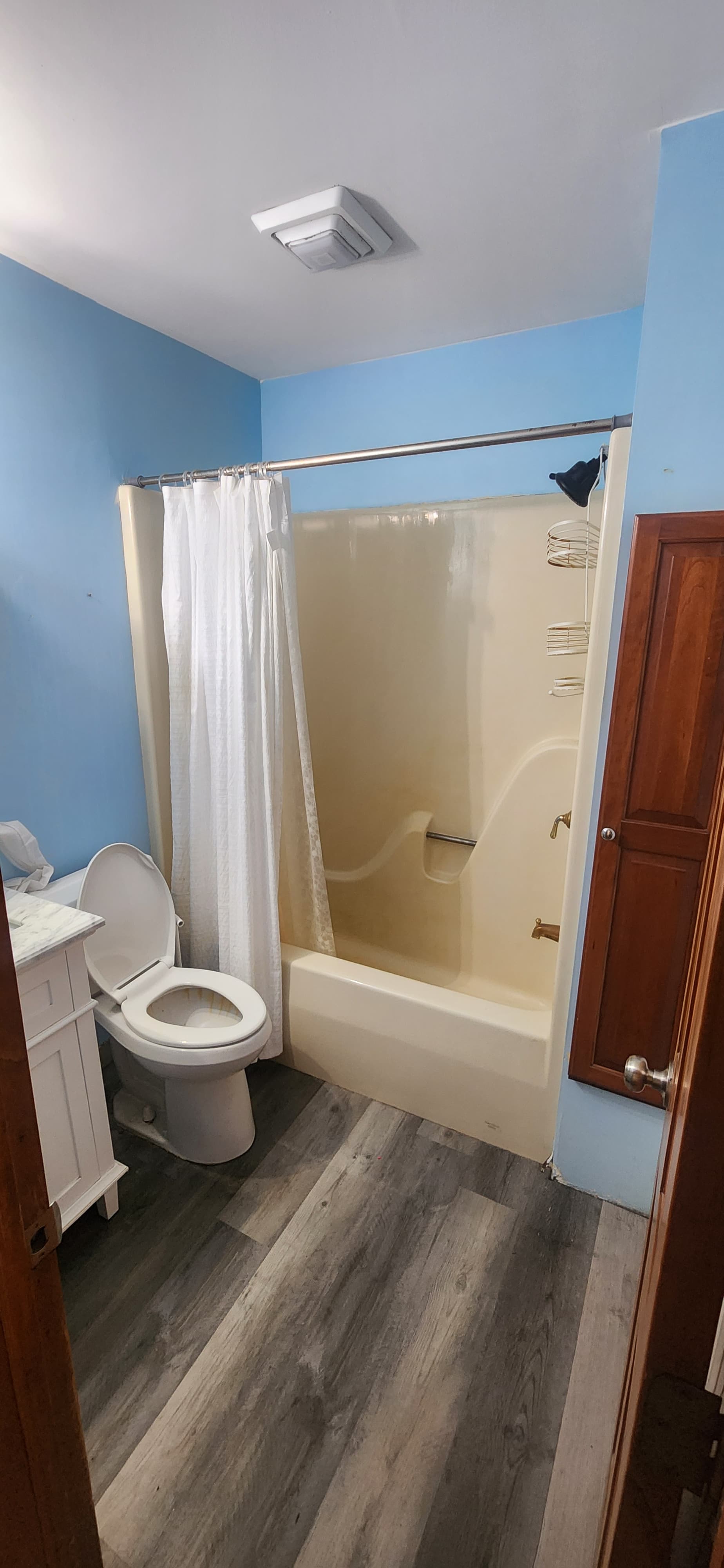 Blue bathroom before renovation with a tub and dark flooring