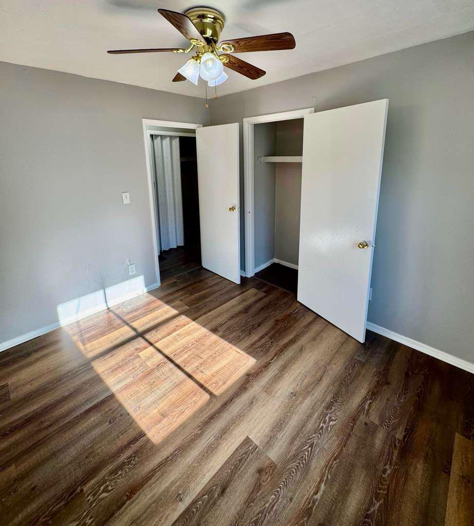 Sunlit bedroom with dark flooring, white trim and double closets