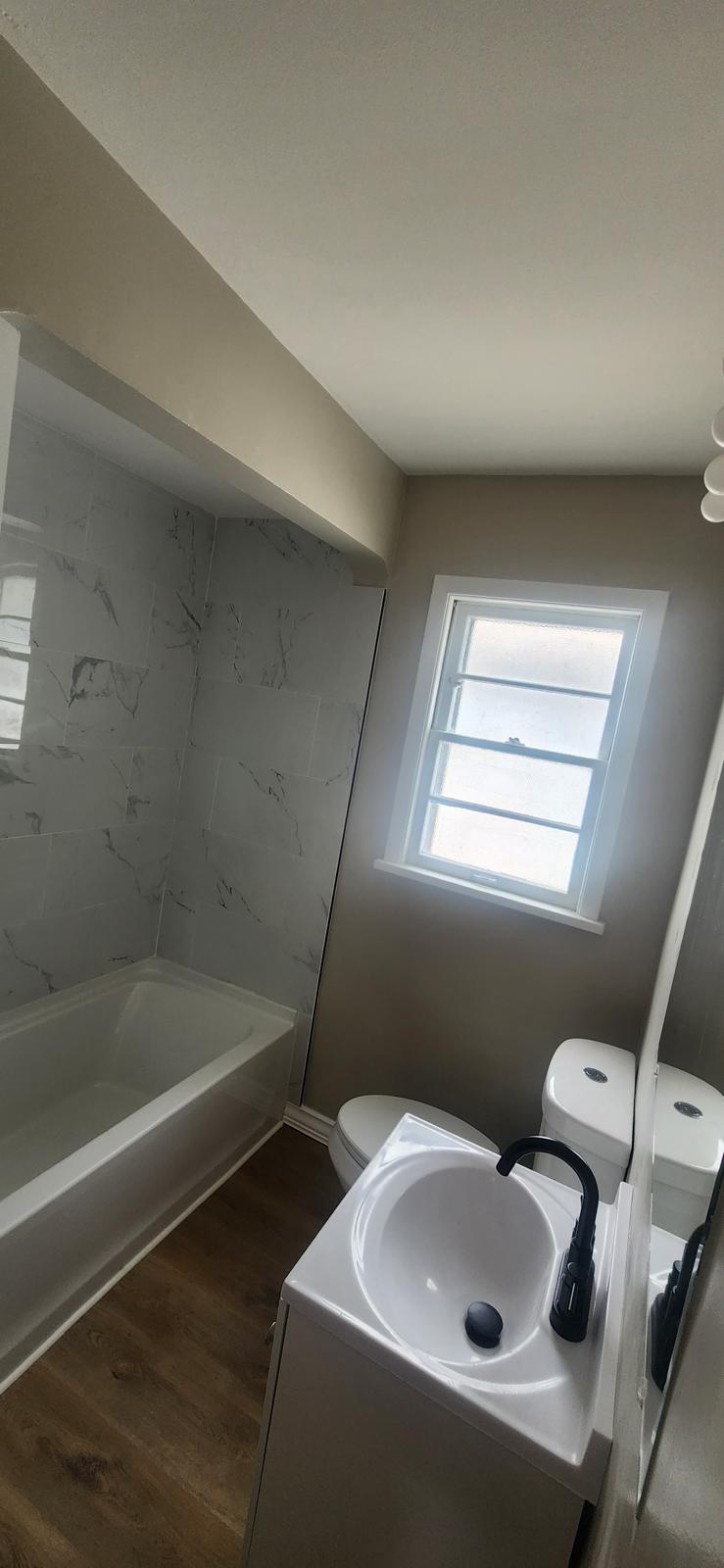 Compact bathroom refreshed with a tub shower, neutral walls and dark flooring