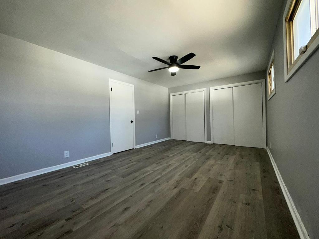 Finished bedroom with gray walls, plank flooring and a black ceiling fan