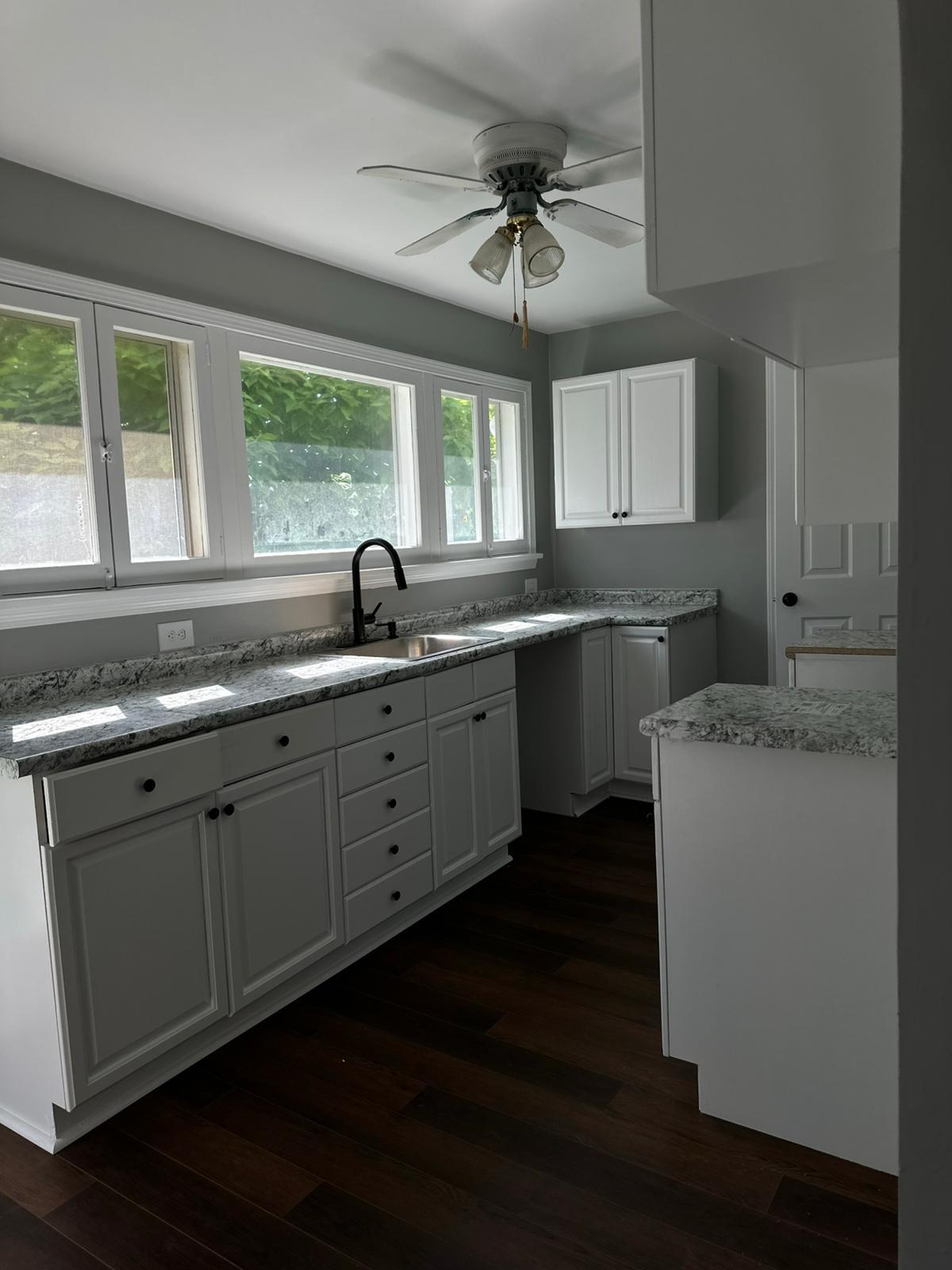 Remodeled gray kitchen with light counters and dark hardwood flooring