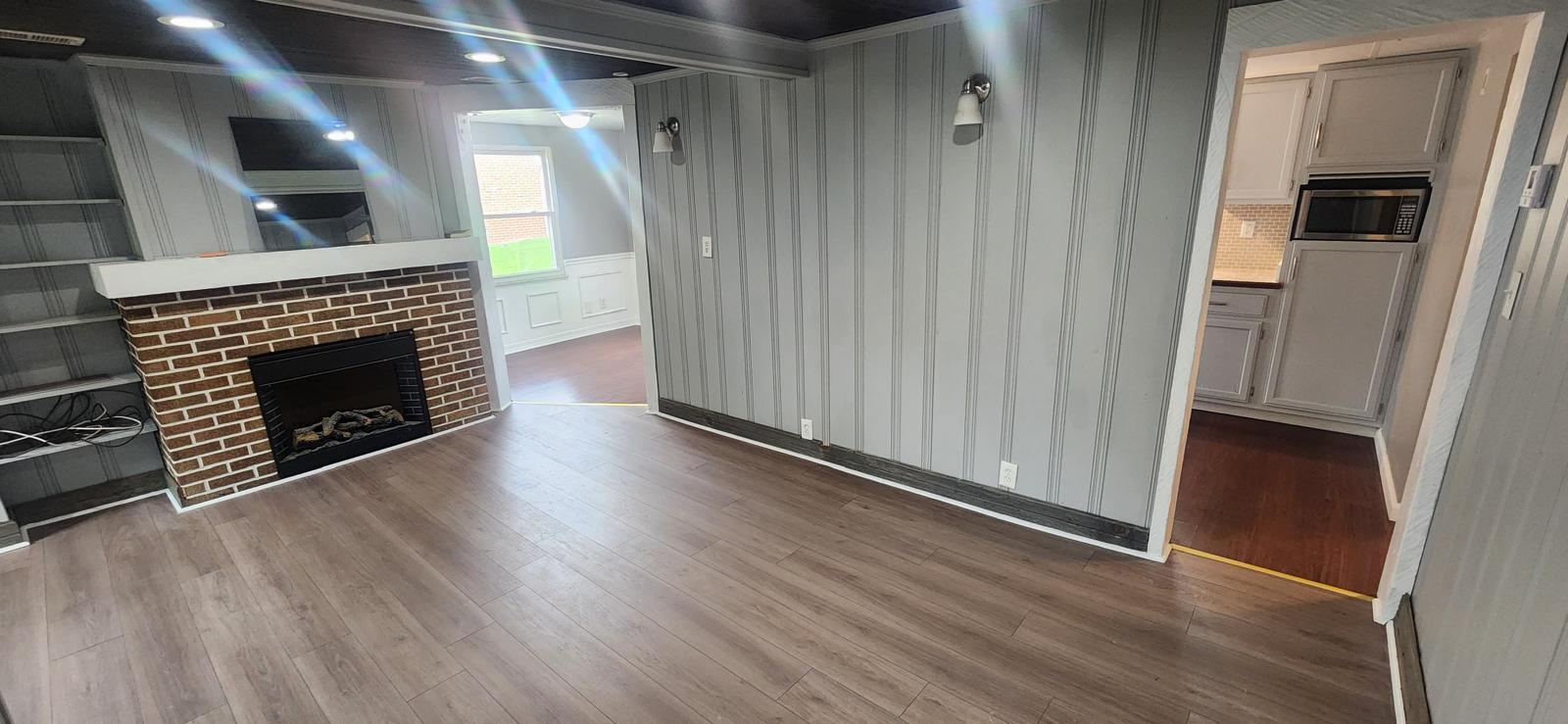 Finished living room with painted paneling, brick fireplace and plank flooring
