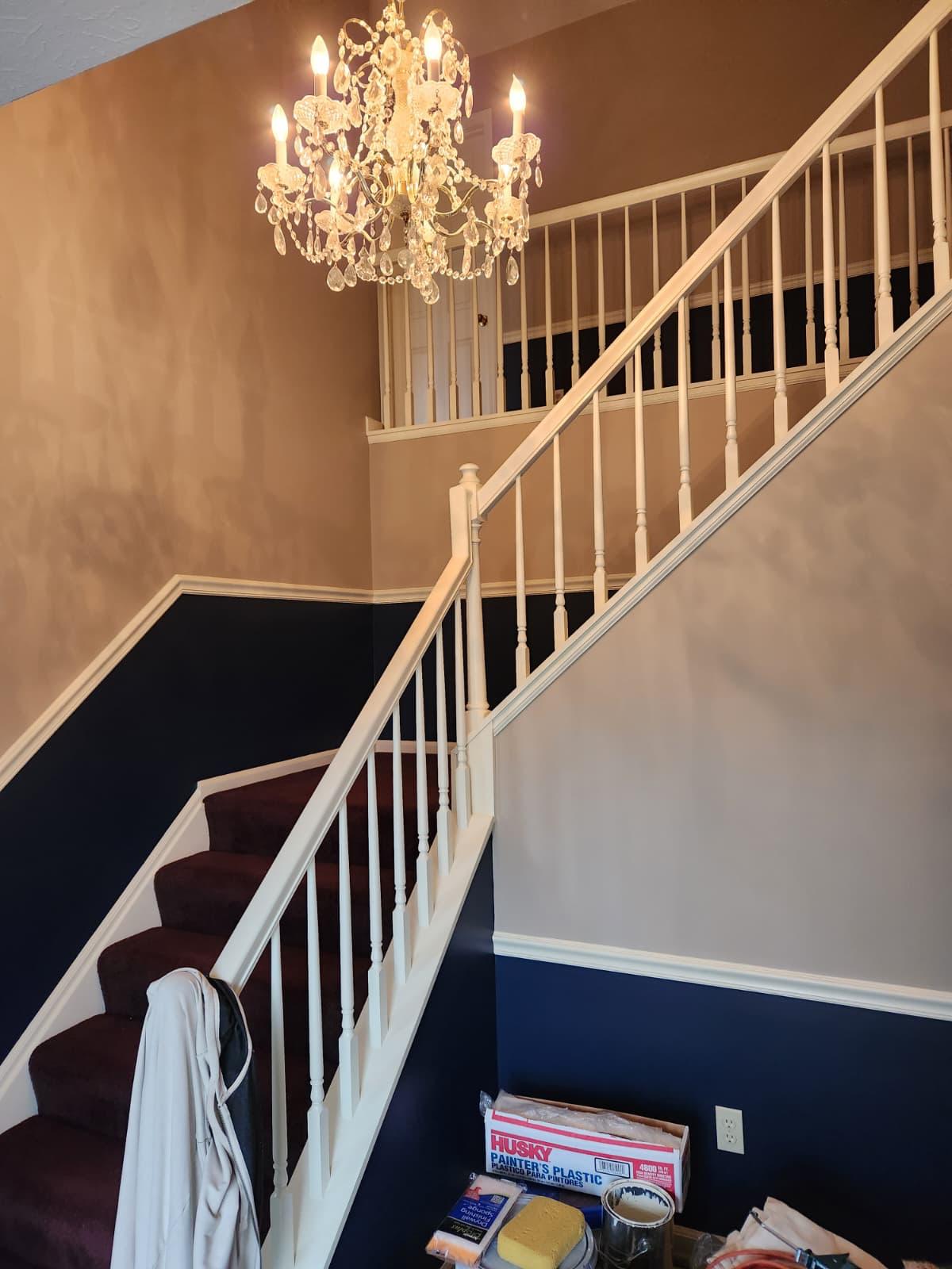 Staircase with a navy accent wall, white railing and crystal chandelier