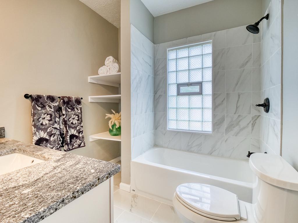 Remodeled bathroom with a tub, marble-look wall tile and updated fixtures