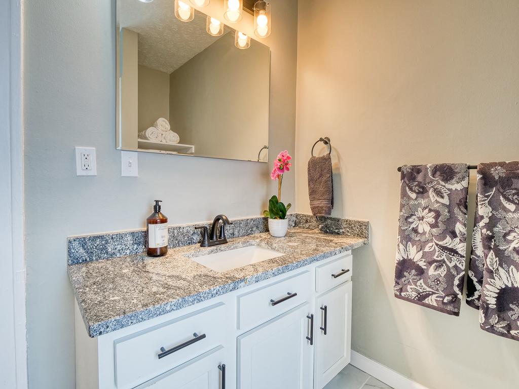 Bathroom vanity with white cabinetry, a stone counter and updated fixtures