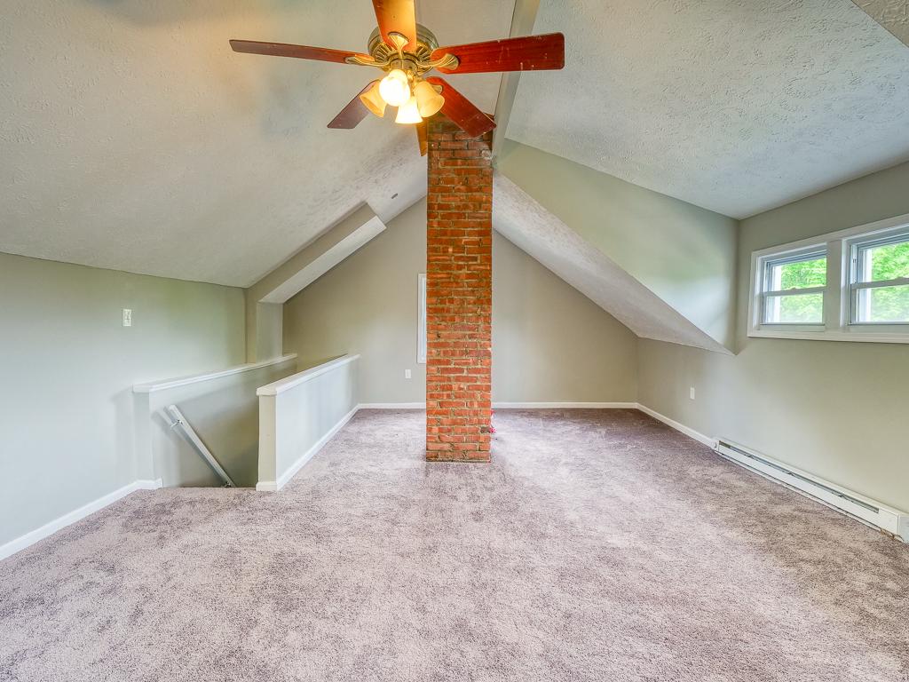 Finished carpeted attic with sloped ceilings and an exposed brick chimney