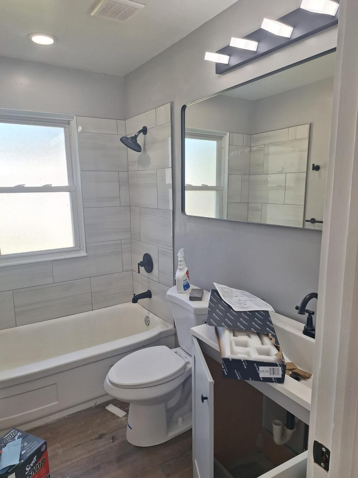 Gray bathroom with a tub shower, updated vanity and dark flooring