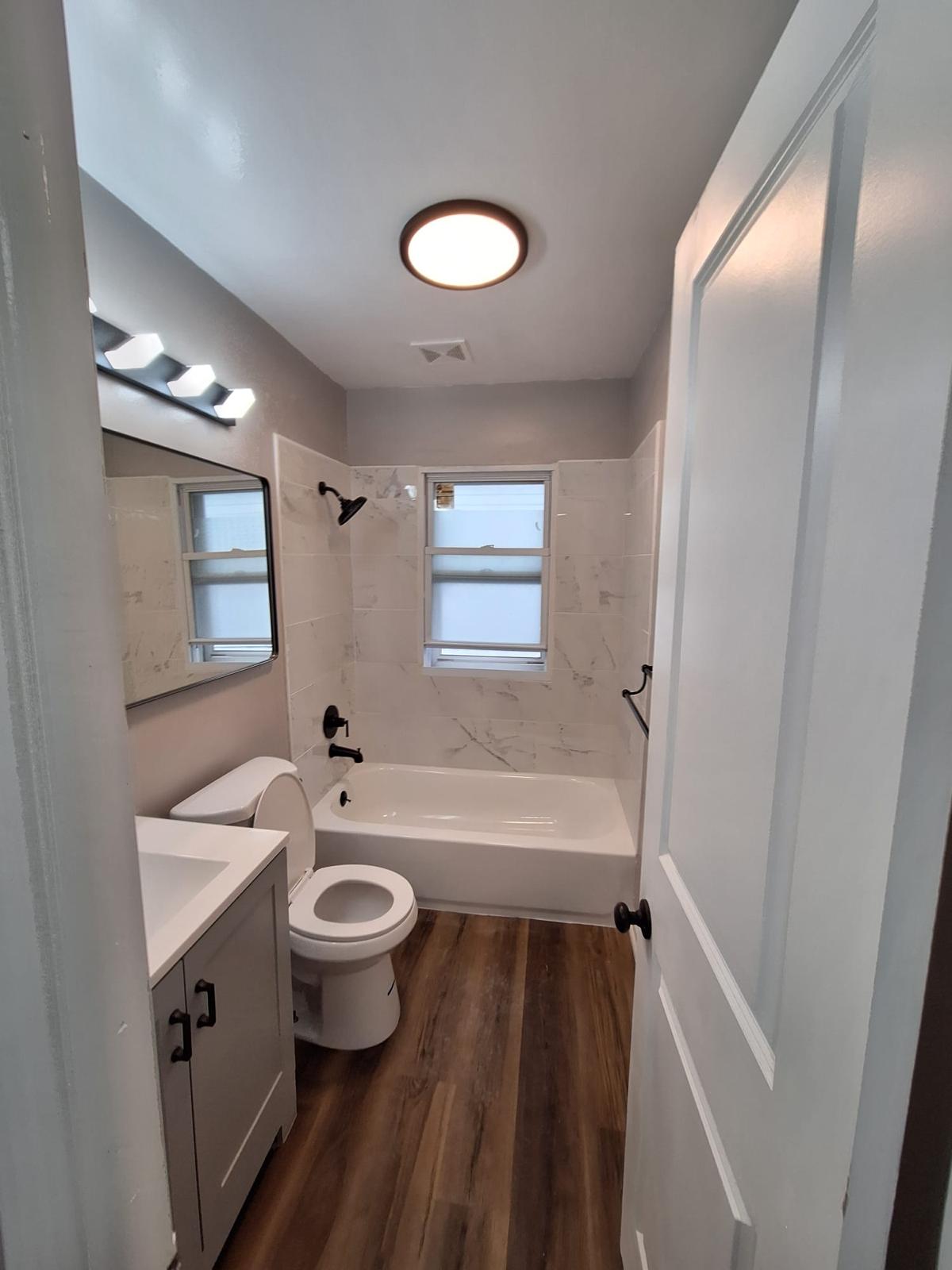Narrow bathroom remodel with a tub shower, updated fixtures and wood-look flooring