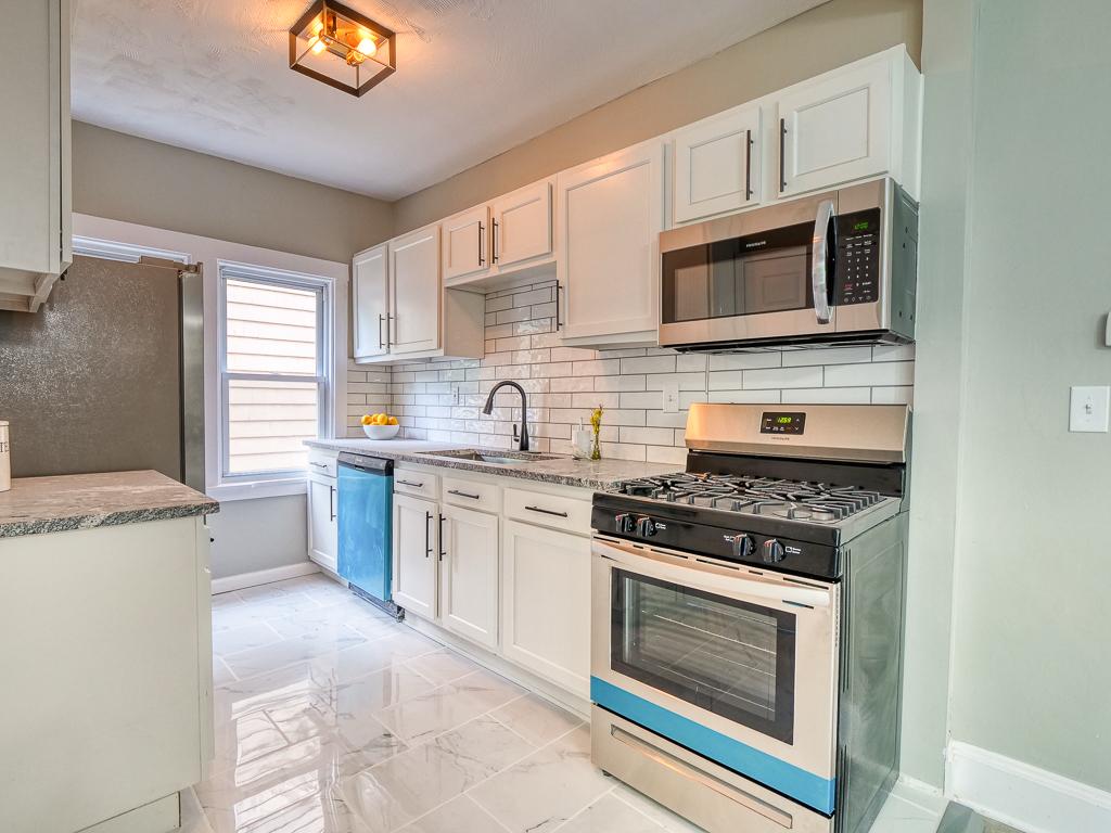 Galley view of a white kitchen with stone counters and subway tile