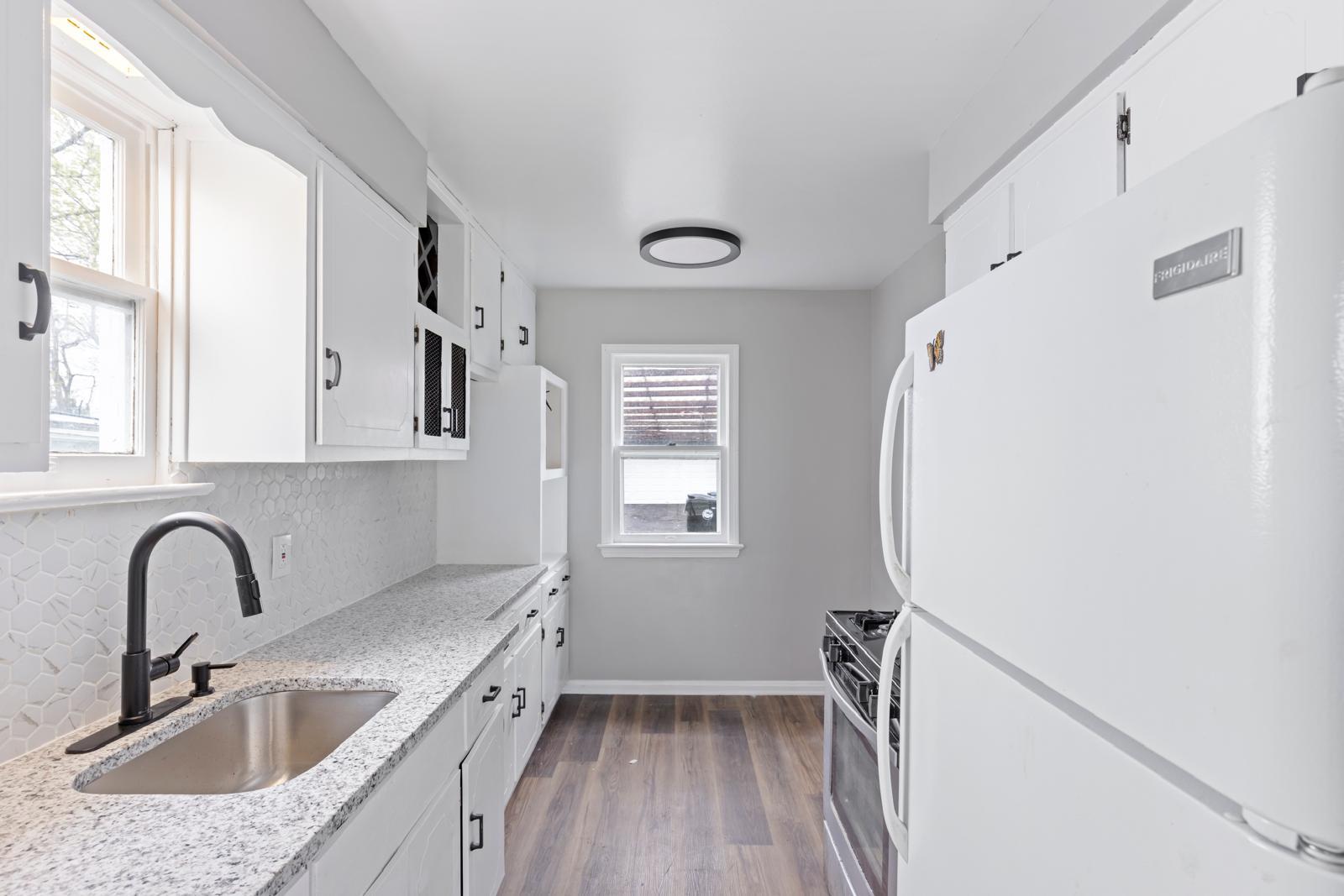 Finished white kitchen with stone counters, a dark faucet and wood-look flooring
