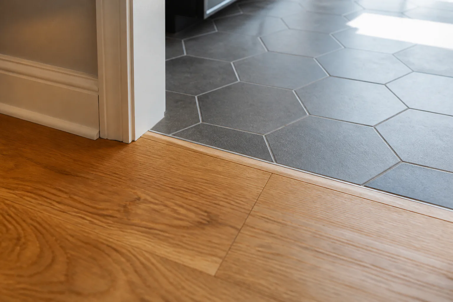 Precise transition from warm oak flooring to charcoal hexagonal tile